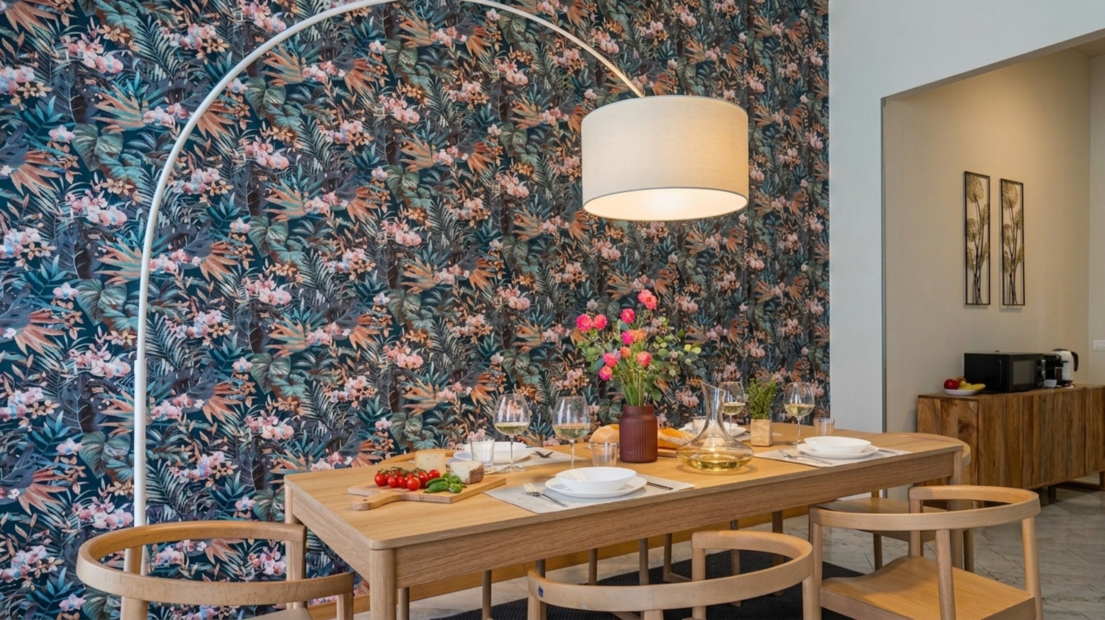 Un comedor con papel tapiz floral, una mesa de madera dispuesta para dos personas y una lámpara moderna.