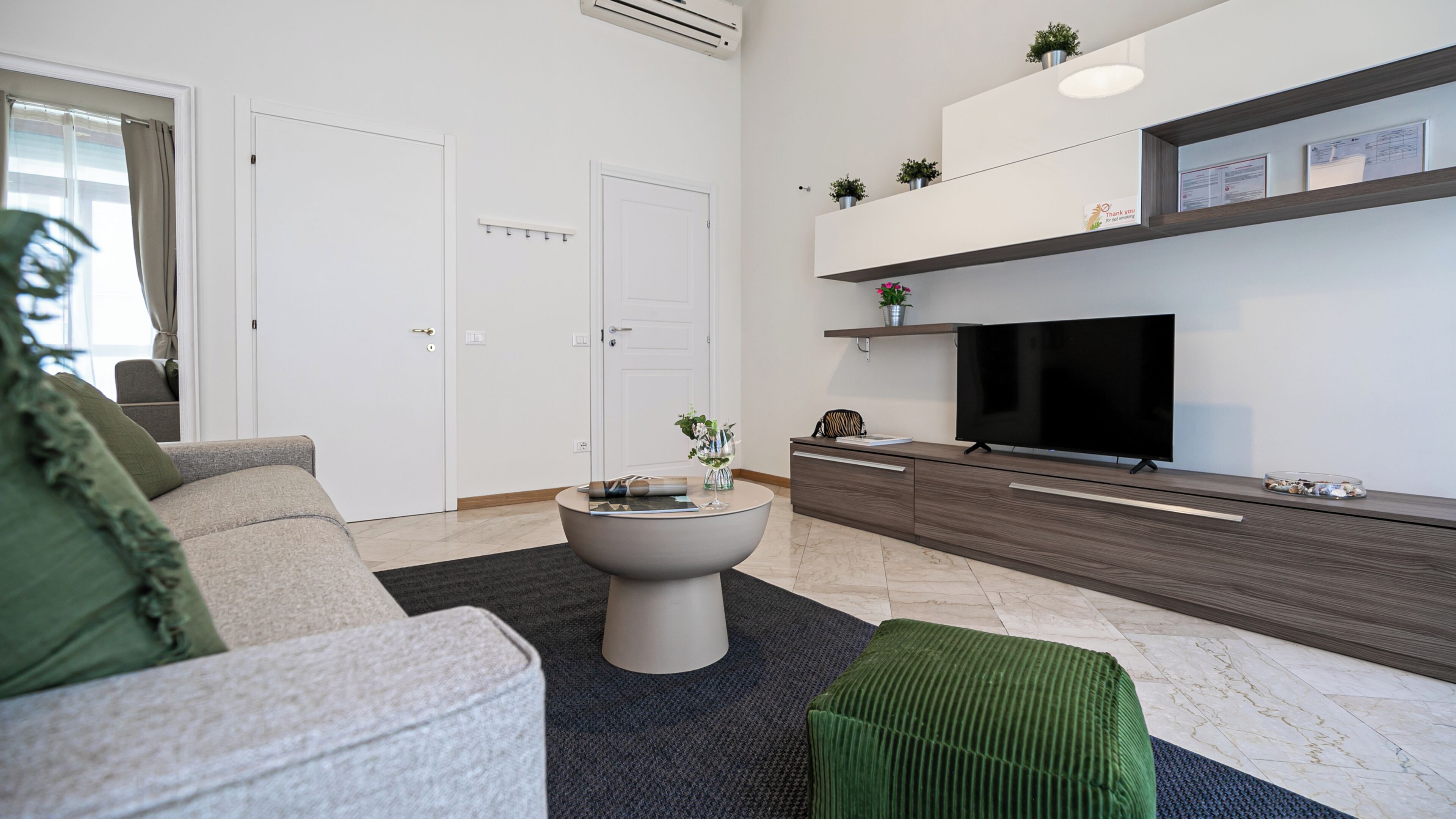 A modern living room with a sofa, a coffee table, a flat-screen TV, and a built-in shelf with plants.