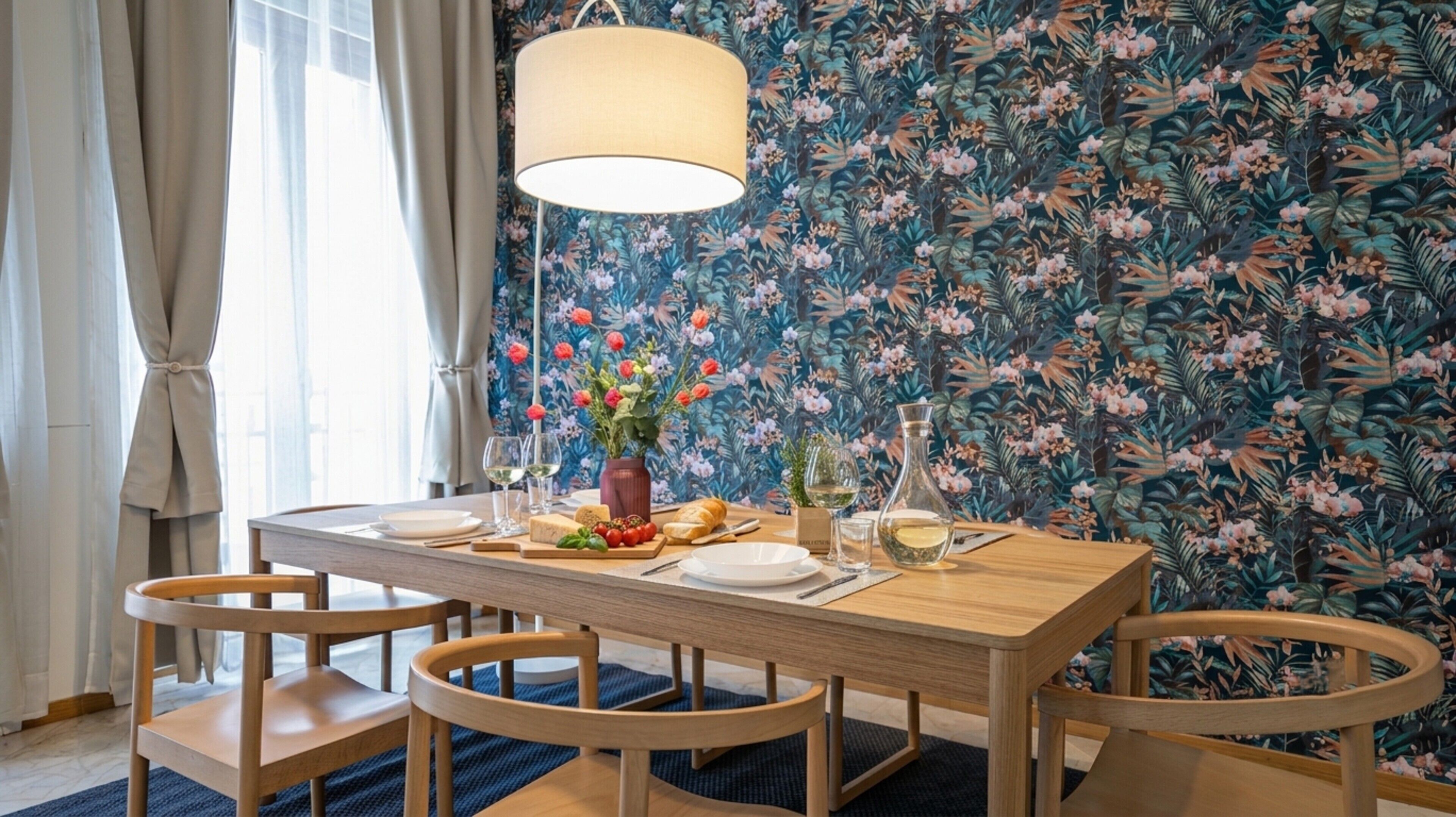 A dining area with a wooden table, chairs, a hanging light fixture, and a floral wallpaper background.