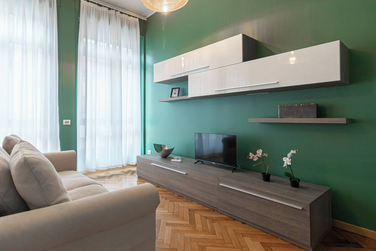 Ein modernes Wohnzimmer mit einer Couch, einem Fernseher und eingelassenen Regalen vor einer grünen Wand.