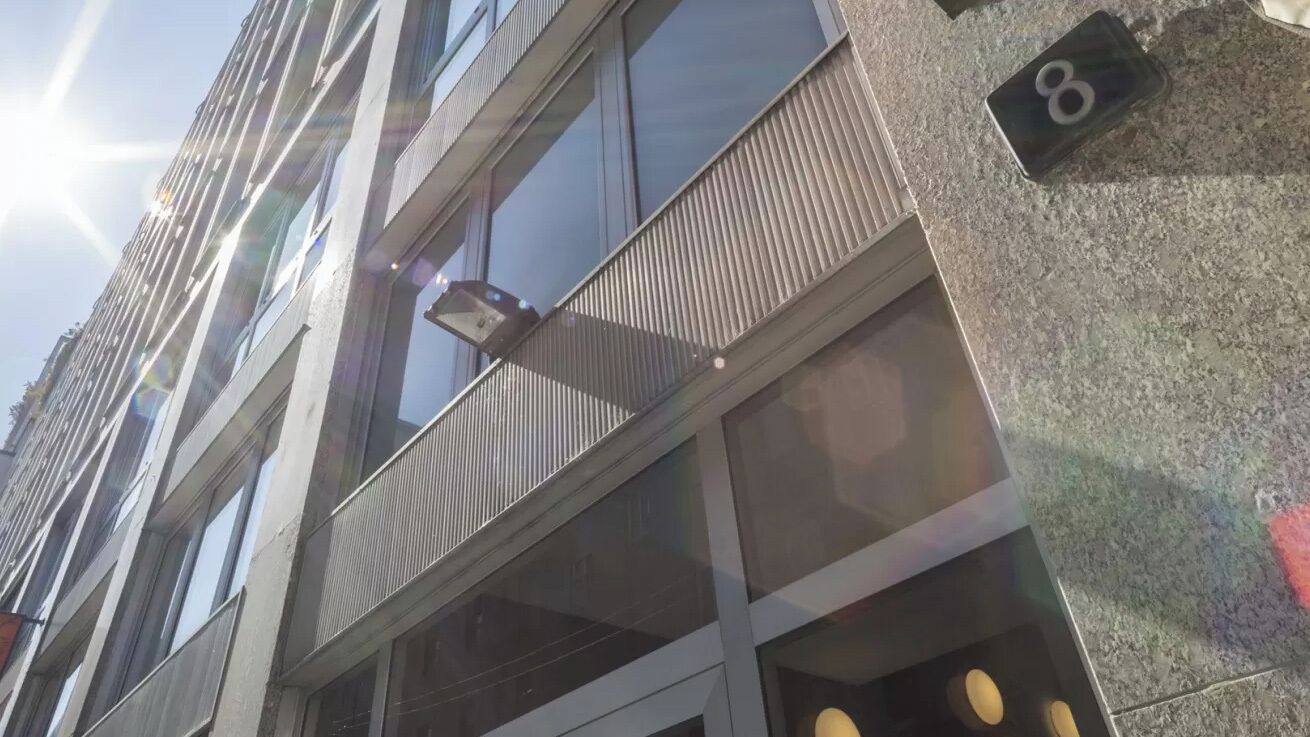 Un edificio moderno con varios pisos, ventanas amplias y un balcón con barandilla de metal.