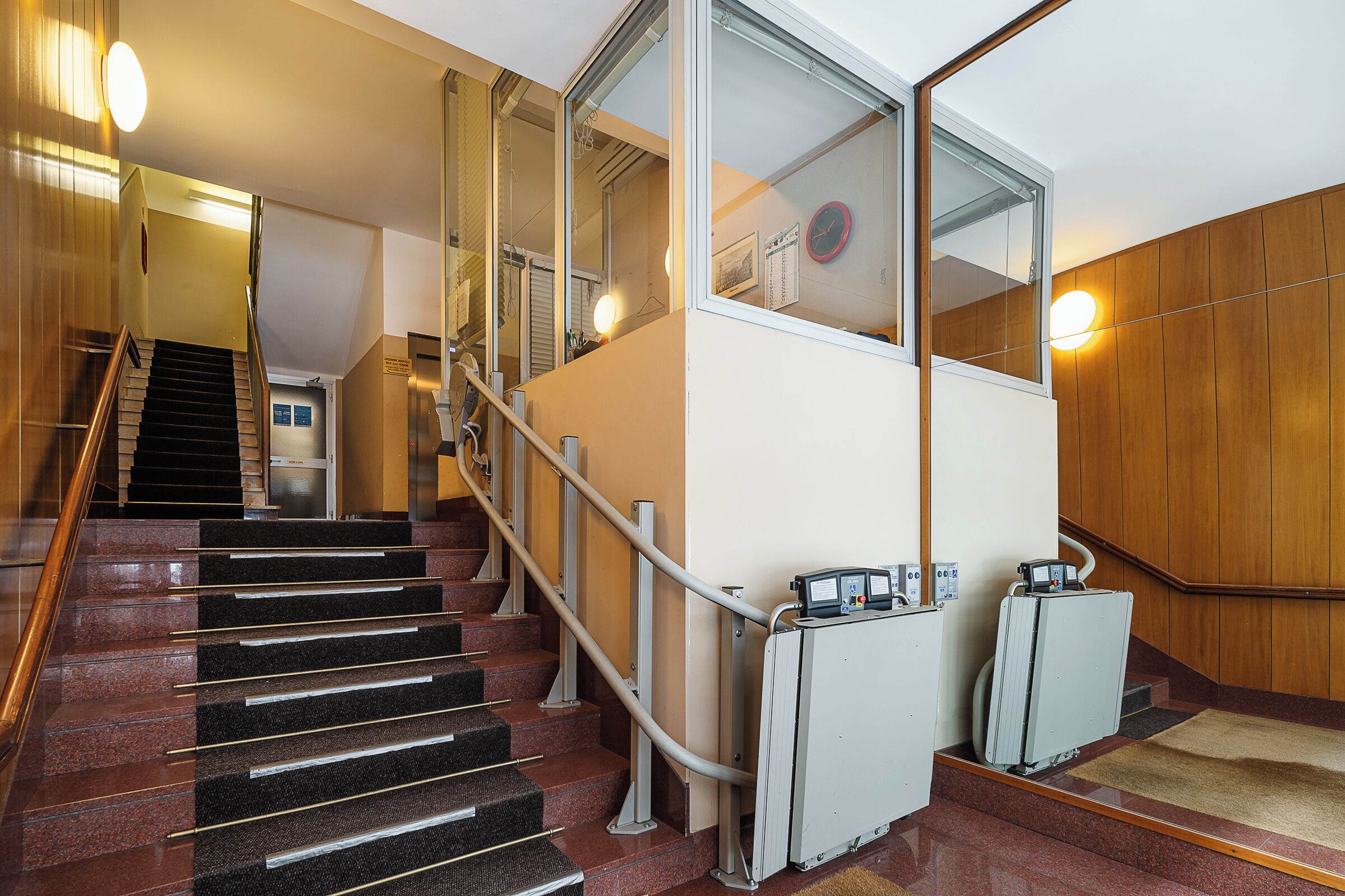 A staircase with a handrail, a glass elevator, and a wall-mounted clock.