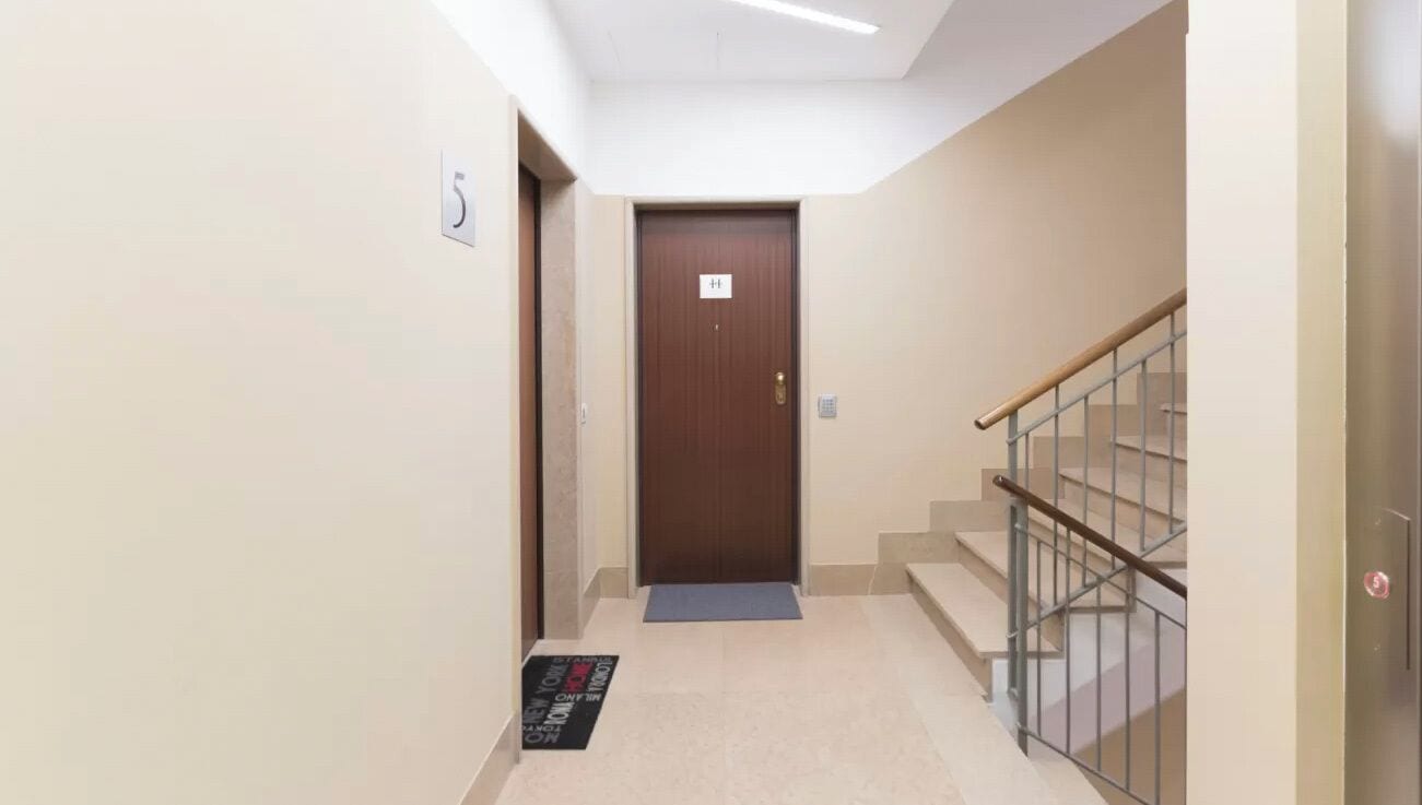 Un pasillo con una puerta marrón, un felpudo y una escalera con barandilla de metal.