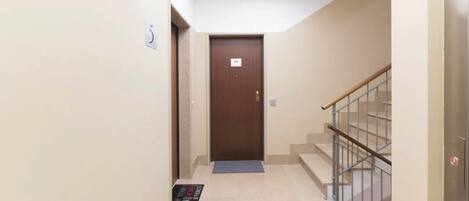 Un pasillo con una puerta marrón, un felpudo y una escalera con barandilla de metal.