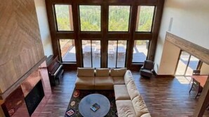 A spacious living room with a large window, a fireplace, and a high ceiling. - Zion Views- Kolob Cabin + Resort Access (Orderville)
