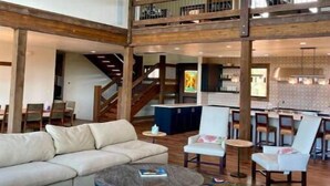 A spacious living area with a large sectional sofa, a coffee table, and a patterned rug. A staircase leads to an upper level with a balcony. - Zion Views- Kolob Cabin + Resort Access (Orderville)