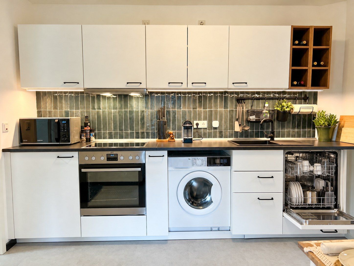 A modern kitchen with white cabinetry, a built-in microwave, oven, and dishwasher, and a backsplash with green tiles.