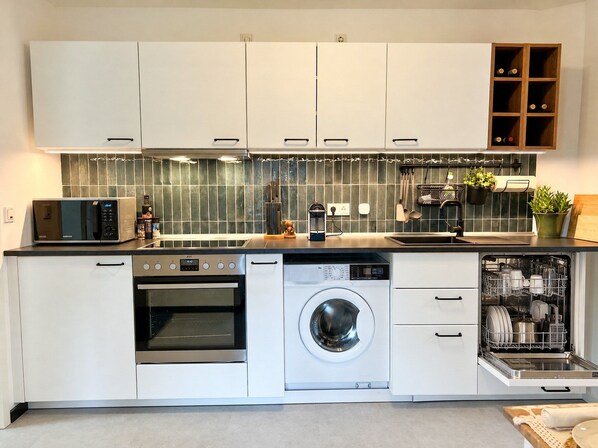 A modern kitchen with white cabinetry, a built-in microwave, oven, and dishwasher, and a backsplash with green tiles. - JUPAS° Soho Home – Studio with Parking (Trier)