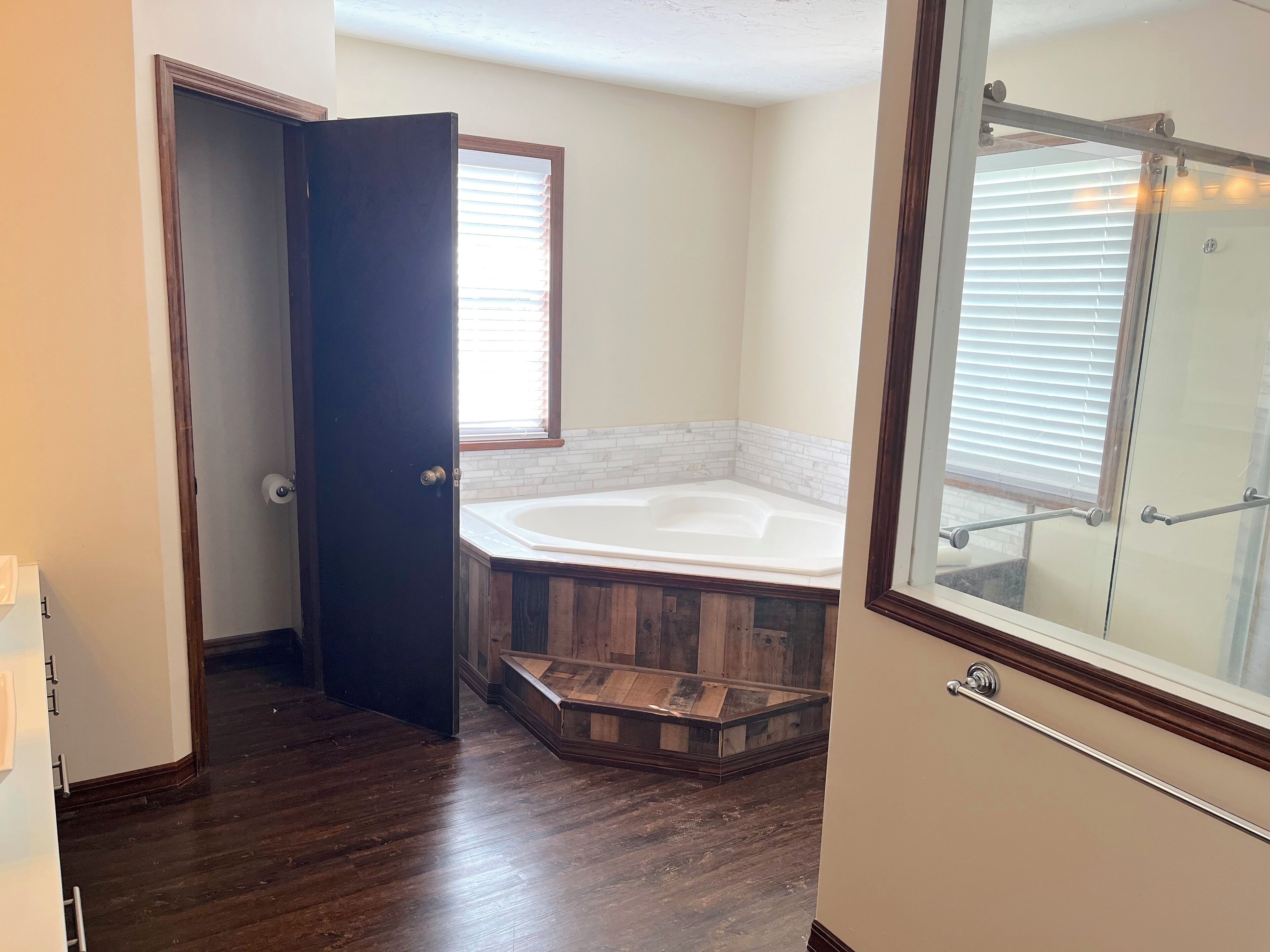 Un baño con piso de madera, una bañera y un box de ducha de vidrio.