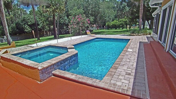 A rectangular swimming pool with a hot tub on one end, surrounded by a brick deck.