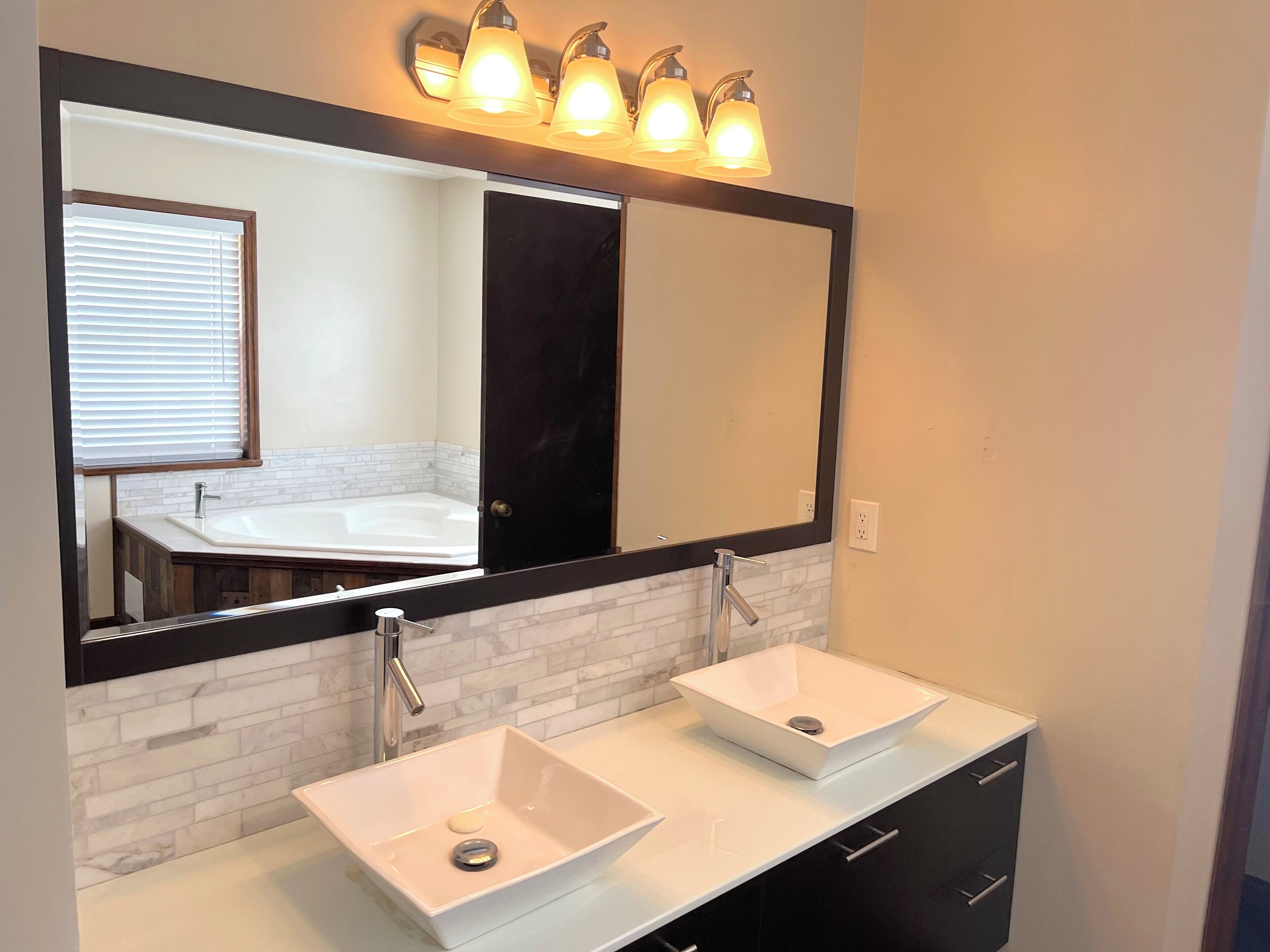 A bathroom with two sinks, a large mirror, and a window with blinds.