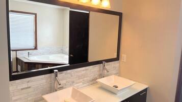 A bathroom with two sinks, a large mirror, and a window with blinds.