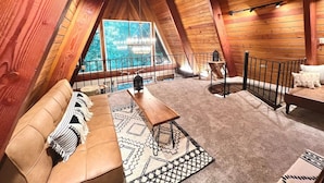 An attic room with a wooden ceiling, a sofa, a table, and a view of the outdoors. - Riverfront A-frame Mt Hood! Skiing*Hiking*Hot tub (Rhododendron)
