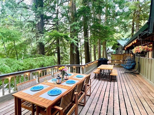 A wooden deck with a dining table set for four, surrounded by chairs.