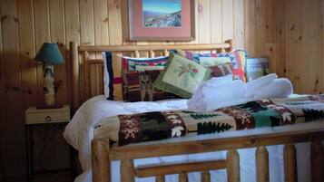 Una habitación de cabaña de madera con una cama, una mesita de noche, una lámpara y un cuadro en la pared.