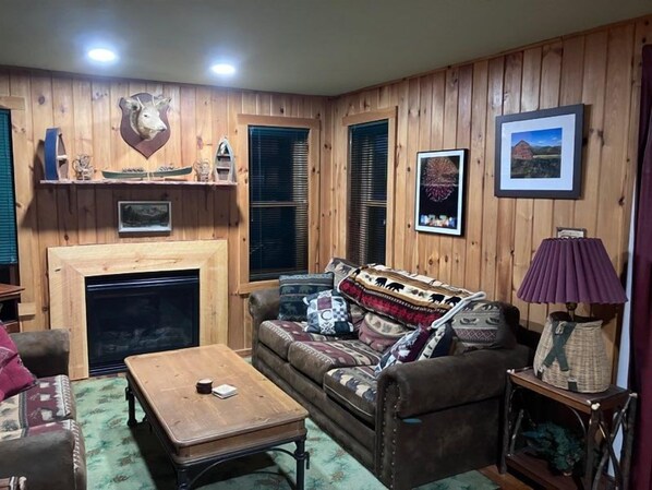 A cozy living room with a fireplace, wooden walls, and a sofa with patterned cushions. - A Private Romantic Waterfront Cabin with hot tub for two (Saranac Lake)