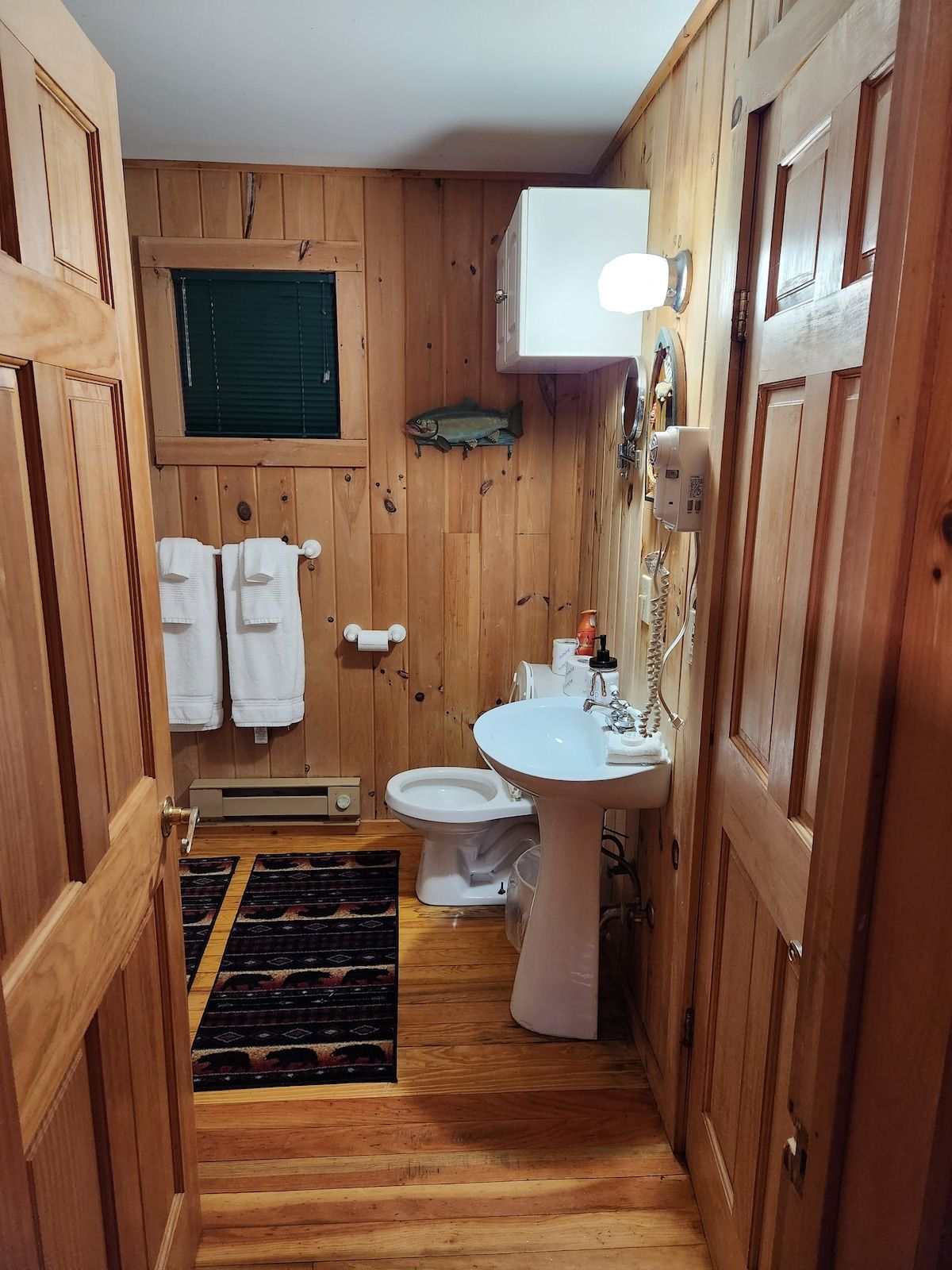 A wooden-paneled bathroom with a toilet, sink, and towel rack.