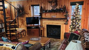 L’intérieur d’un chalet confortable, avec une cheminée, un téléviseur et un sapin de Noël.