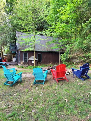 A cabin with a porch, surrounded by trees, and outdoor seating with Adirondack chairs. - A Private Romantic Waterfront Cabin with hot tub for two (Saranac Lake)