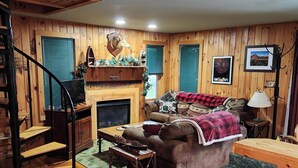 Un intérieur de chalet chaleureux avec une cheminée, des murs en bois, un canapé, une table à manger et un coin cuisine.