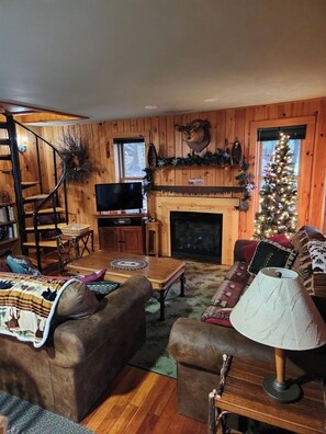 Ein gemütliches Blockhaus-Interieur mit Kamin, Holzwänden, Fernseher und Weihnachtsbaum.