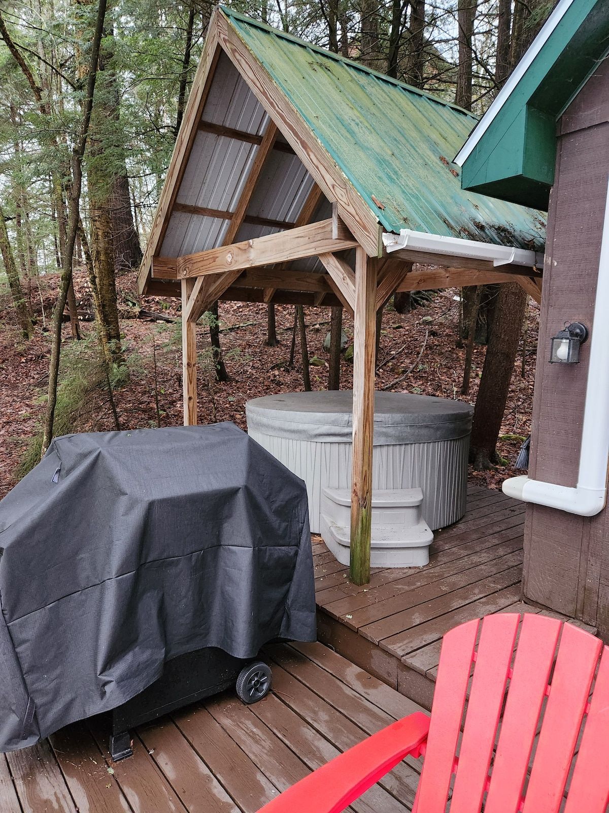 A wooden deck with a covered grill, a hot tub, and a red chair.