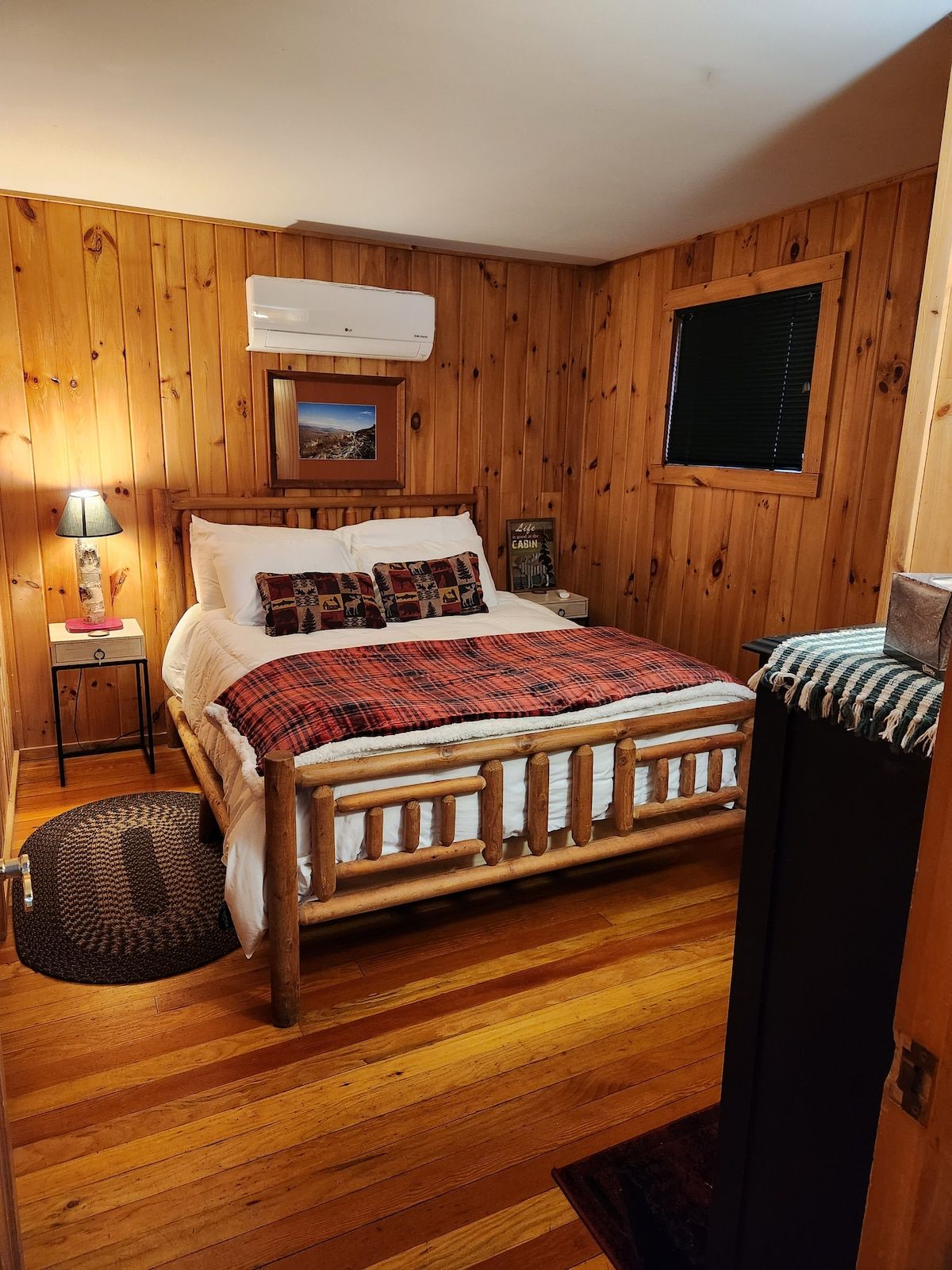 A wooden-paneled room with a bed, a nightstand, a lamp, and a window.