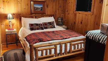 A wooden-paneled room with a bed, a nightstand, a lamp, and a window.