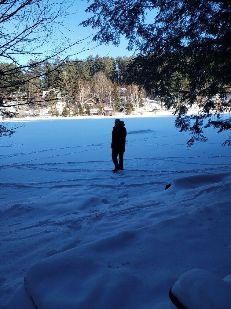 A person standing in a snowy outdoor area with trees and houses in the background.