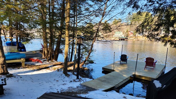 Un chalet au bord du lac, avec un quai, une chaise et un banc.
