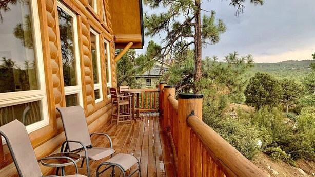 A wooden deck with chairs and a table, overlooking a forested landscape.