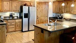 A kitchen with wooden cabinets, a stainless steel refrigerator, a granite countertop, and pendant lighting.