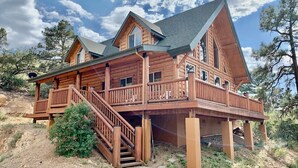 A log cabin with a balcony, a staircase, and a view of the surrounding landscape.