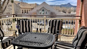 A balcony with a table and chairs, a view of a building labeled "SOLID ROCK," and a mountain in the background. - The 1900 House - 1 Block From DT (Prescott)