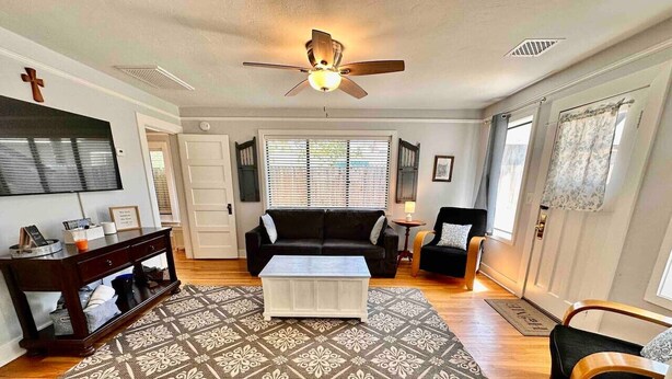 Un salon avec un ventilateur de plafond, un canapé, une table basse et un tapis à motifs.