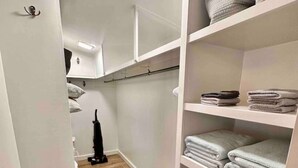 Un couloir étroit doté d’un plancher en bois, de murs blancs et d’un placard avec des étagères où sont rangées des serviettes pliées et un panier.
