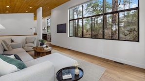 A modern living room with a large window, a wooden ceiling, and a cozy seating area. - Prescott Treehouse. Luxe 4BR/3Ba Home. Sleeps 10 (Prescott)