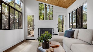 A modern living room with a fireplace, large windows, and a cozy sofa. - Prescott Treehouse. Luxe 4BR/3Ba Home. Sleeps 10 (Prescott)