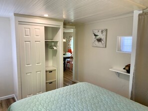Un dormitorio con una cama, un armario, una estantería pequeña y un cuadro en la pared.