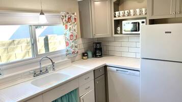 A compact kitchen with a sink, a microwave, and a refrigerator. There is a window with a curtain, and a coffee maker is visible on the countertop.