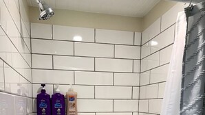 Un espace douche avec des carreaux blancs, une pomme de douche et deux bouteilles de shampoing posées sur une étagère.