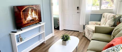 Un salon avec un téléviseur posé sur un meuble blanc, une table basse blanche ornée d’une plante, un canapé vert et une porte blanche.