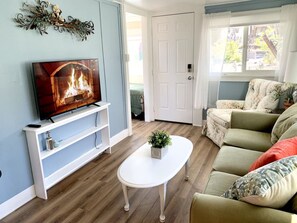 A living room with a TV on a white stand, a white coffee table with a plant, a green sofa, and a white door. - Downtown Birdie / walk to whiskey row (Prescott)