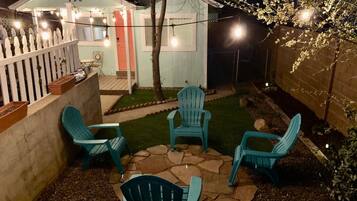 Un patio trasero con área de terraza que incluye cuatro sillas y una mesa, rodeado por una cerca blanca de piquete y un cobertizo pequeño con el número 720.