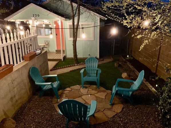 A backyard with a patio area featuring four chairs and a table, surrounded by a white picket fence and a small shed with the number 720 on it.