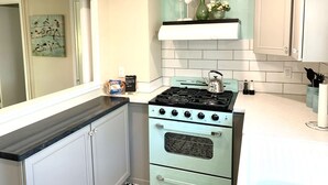Une cuisine avec un four d’époque, des armoires blanches et un pare-feu turquoise.