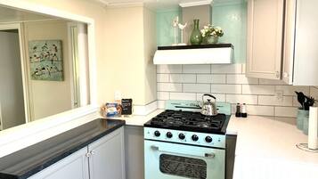 Una cocina con estufa antigua, armarios blancos y salpicadero color turquesa.