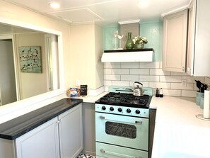 Una cocina con estufa antigua, armarios blancos y salpicadero color turquesa.