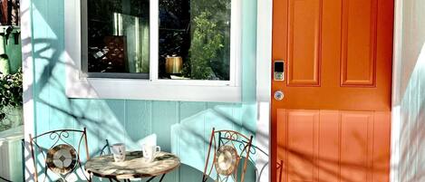 A porch with a table and two chairs, a window, and an orange door.