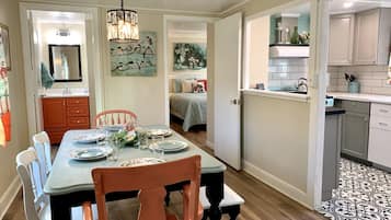 A dining area with a table set for four, a chandelier, and a view into a bedroom.